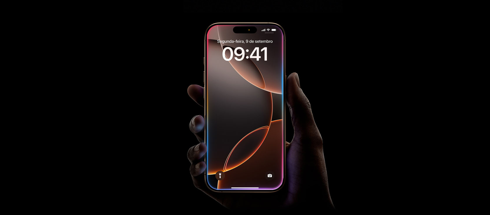Uma mão segura um iPhone 16 Pro na cor titânio-deserto, tela de ponta a ponta, Dynamic Island centralizada na parte superior, cantos arredondados