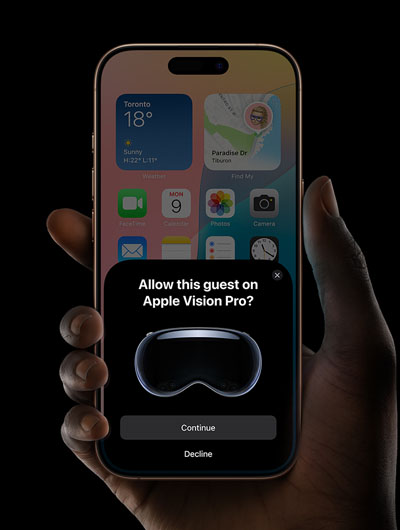 A hand holding an iPhone. The iPhone's screen displays a window with the message, "Allow this guest on Apple Vision Pro?" with buttons labelled "Continue" and "Decline."
