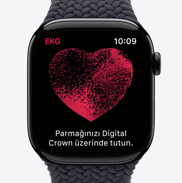 Apple Watch Series 10 üzerinde, içinde parçacıkların hareket ettiği bir kırmızı kalp bulunan EKG uygulaması. “Parmağınızı Digital Crown üzerinde tutun.” yazıyor.