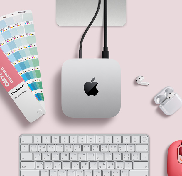 擺放在桌面的銀色 Mac mini 俯視圖,旁邊放著 AirPods、粉紅色無線鍵盤、粉紅色無線滑鼠,以及一組呈扇狀打開的色卡