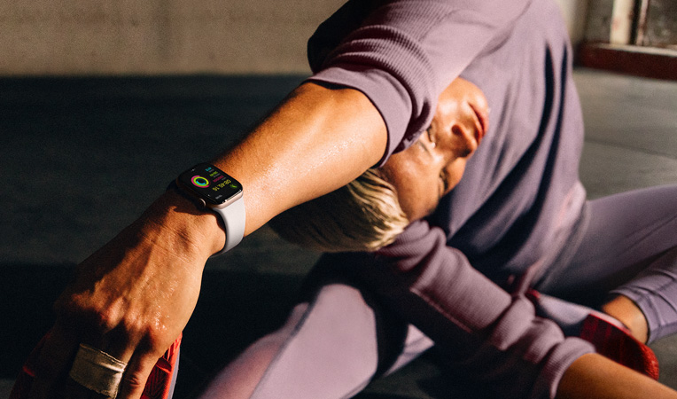 A woman on the floor stretching her arm to her leg while wearing an Apple Watch Series 10, screen shows Workout, Cooldown, Activity, Activity Rings