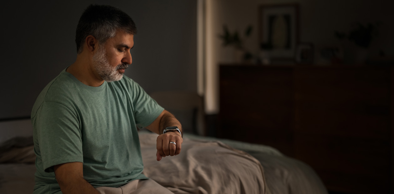 A man sitting in bed checking his Apple Watch.