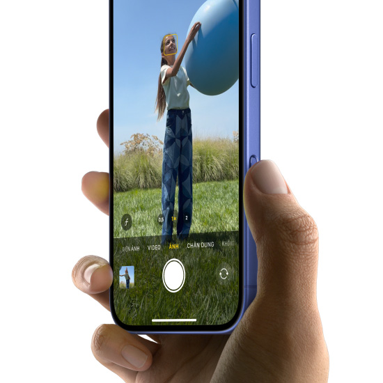 Bàn tay cầm một chiếc iPhone 16 màu Xanh Lưu Ly, với ngón tay cái trượt dọc theo nút Điều Khiển Camera để chọn tính năng Ảnh